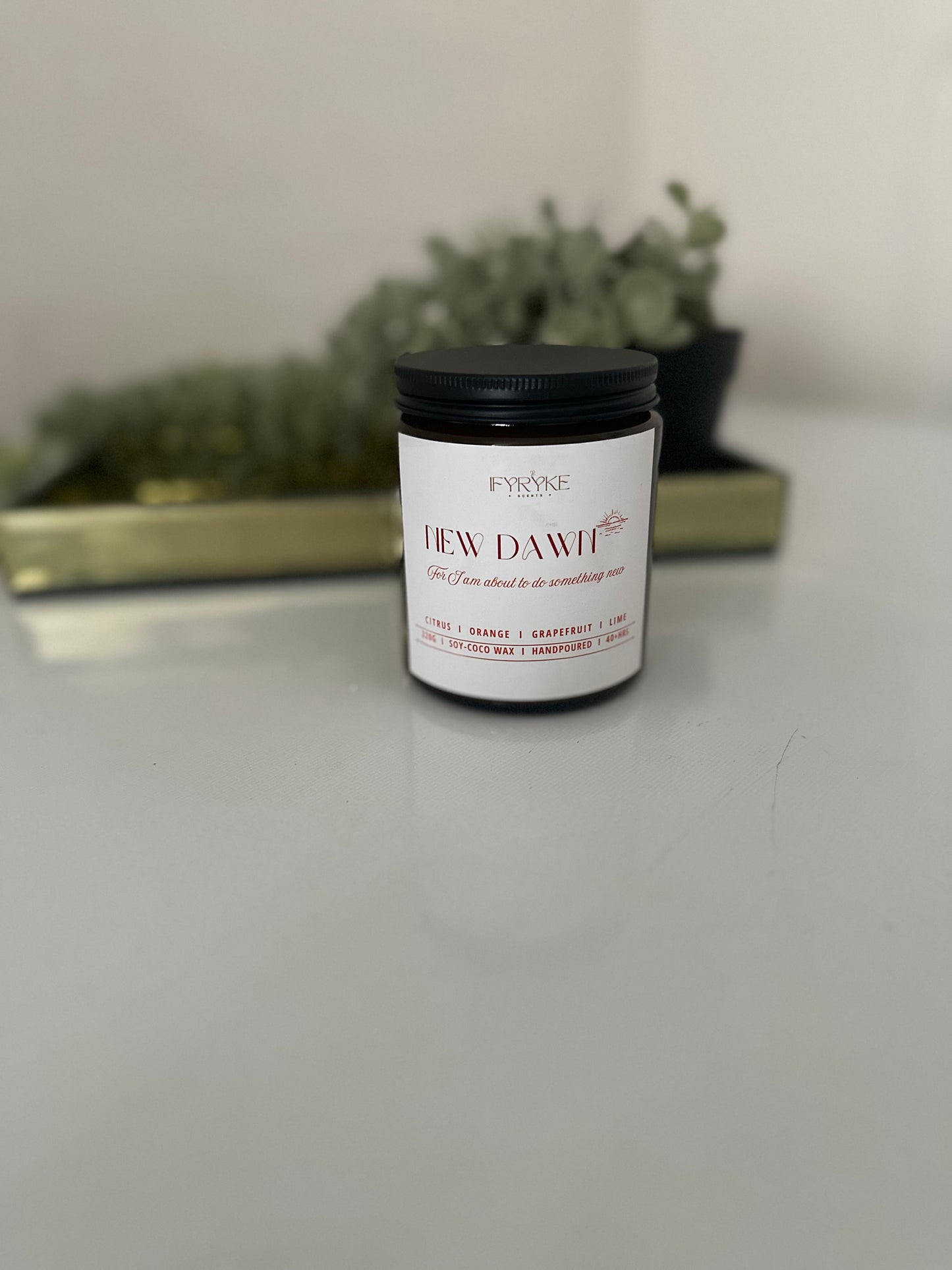 Candle jar labeled 'New Dawn' on a white surface with a blurred background