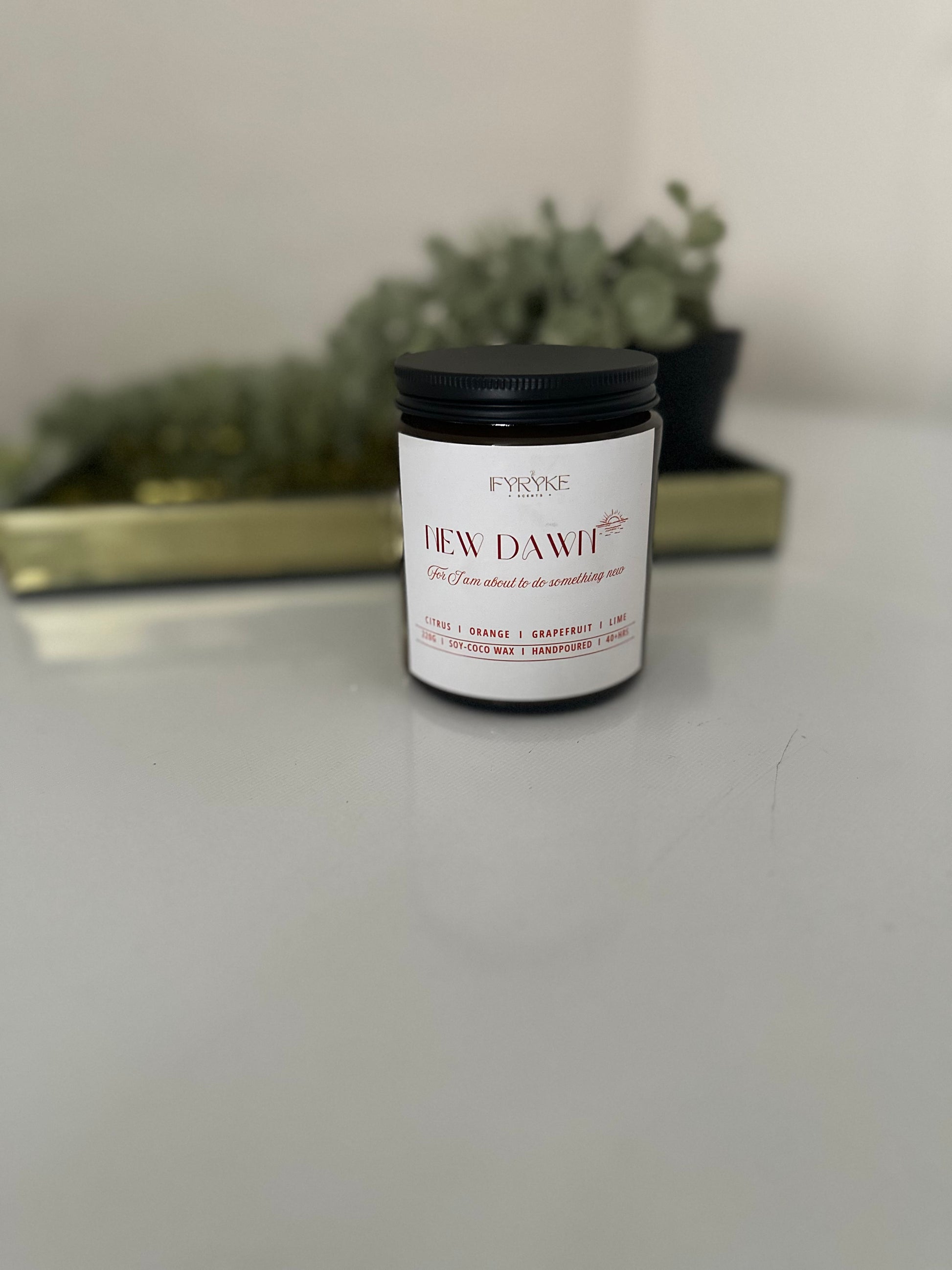 Candle jar labeled 'New Dawn' on a white surface with a blurred background